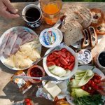 Enjoy a delightful outdoor brunch with bread, cheese, cold cuts, coffee, and fresh vegetables.