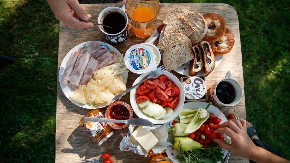 Enjoy a delightful outdoor brunch with bread, cheese, cold cuts, coffee, and fresh vegetables.